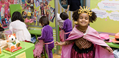 Smiling girl in a pink cape and crown at a museum exhibit